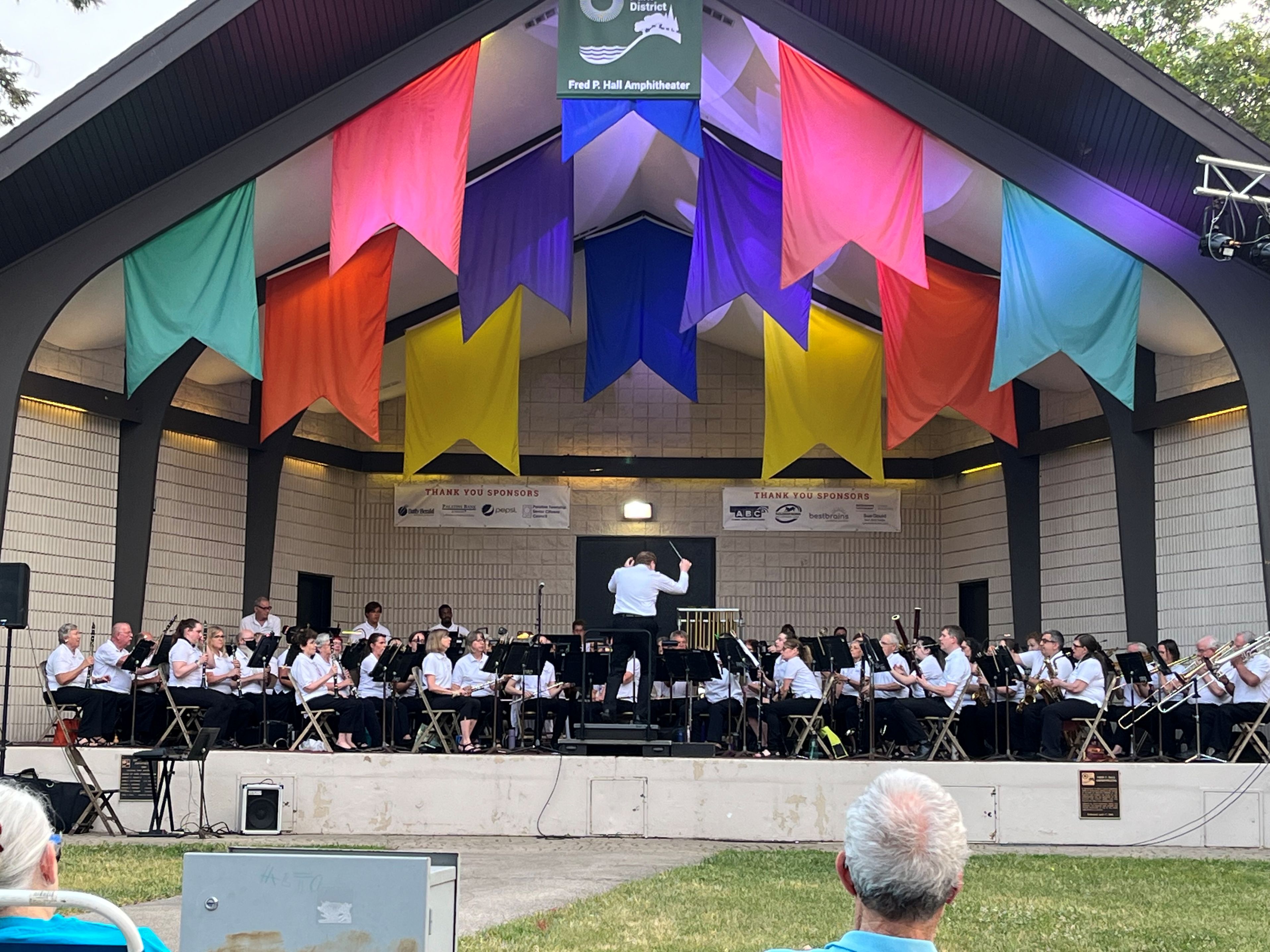 photograph of the full band in mid-performance on the Fred P. Hall Amphitheater outdoor stage in Palatine, IL